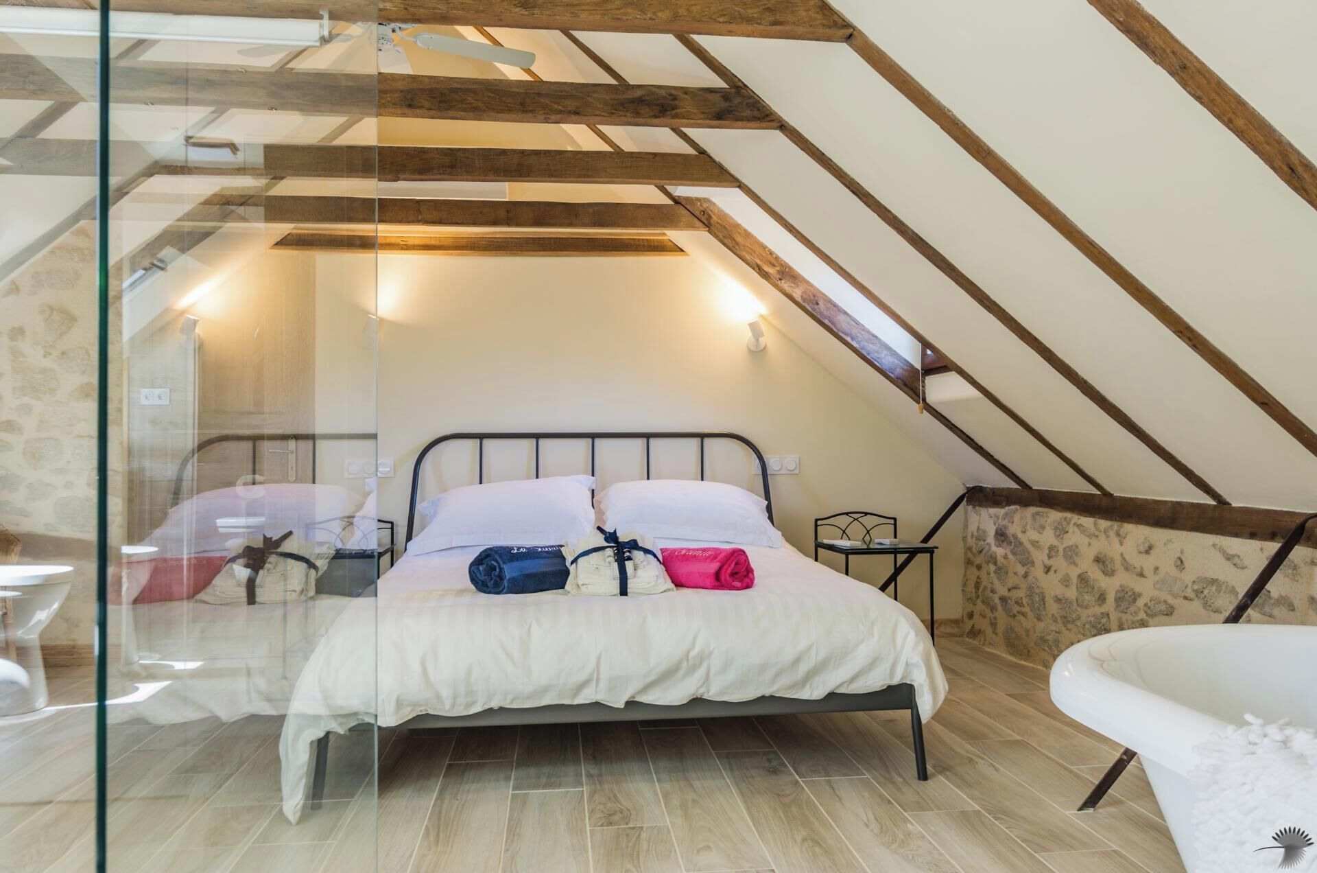 A bedroom with a sloped ceiling, a bed with white bedding, a small bedside table, and a chair.