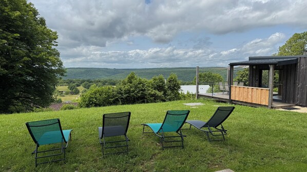 A grassy outdoor area with three lounge chairs and a wooden deck overlooking a scenic landscape.