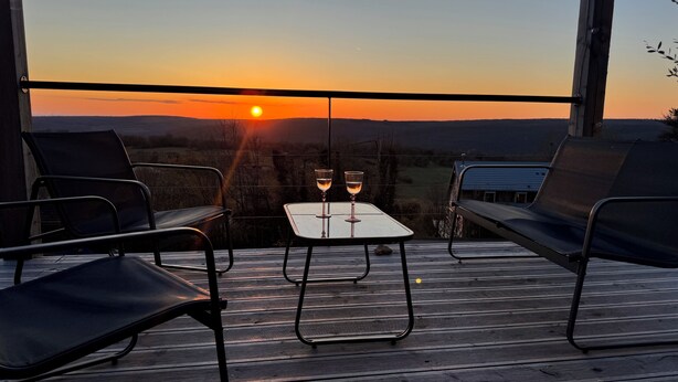 A balcony with two chairs and a table, two glasses of wine, and a sunset view.