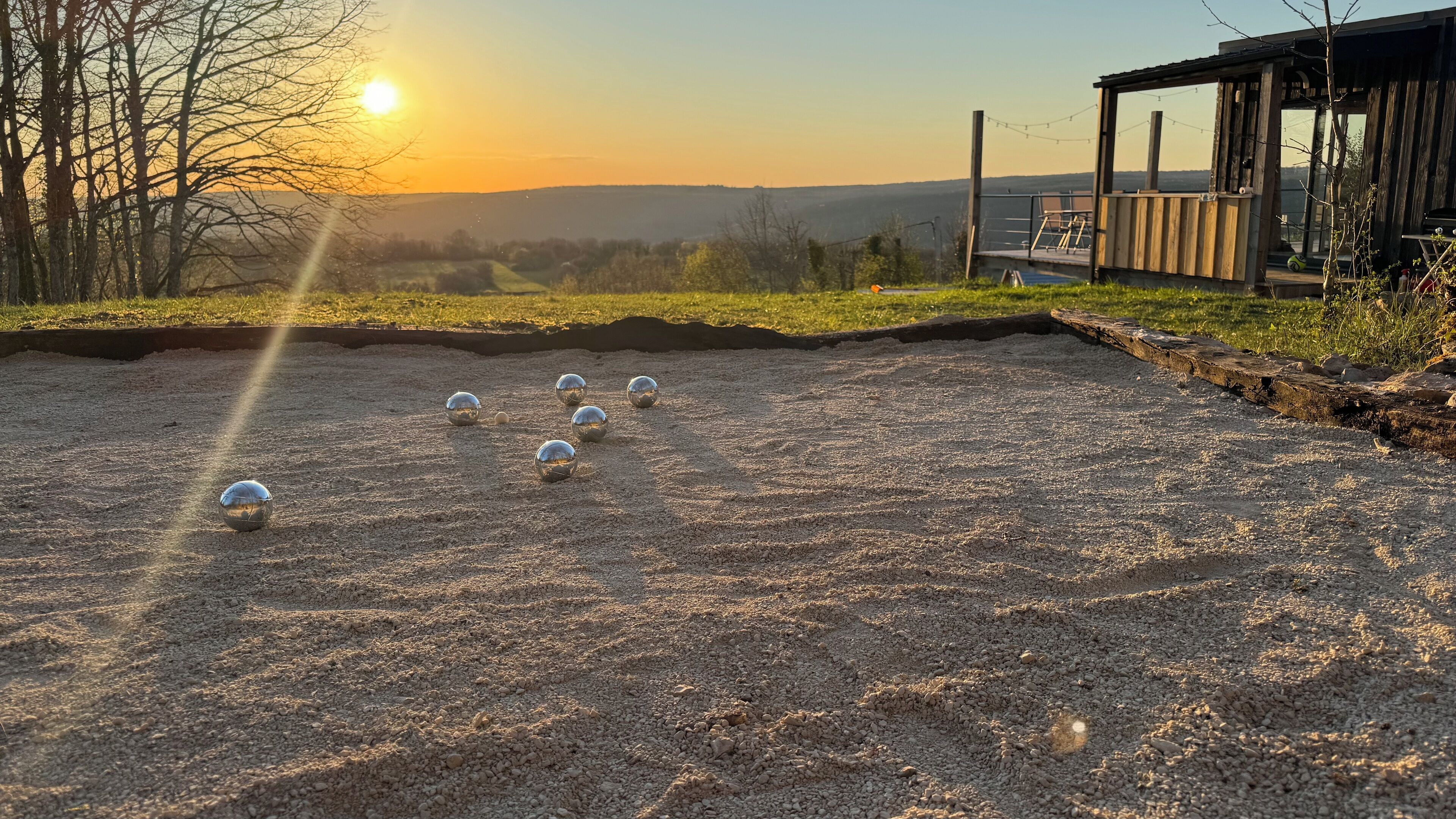 A croquet field with balls and a wooden structure with a deck.