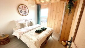 A bedroom with a bed, pillows, a bedside table, a framed picture, a window, and a door.