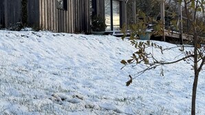 Een houten blokhut met grote ramen en een schuin dak, omgeven door sneeuw bedekte grond en bomen.