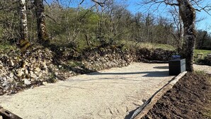 A concrete patio area with a stone border, surrounded by trees and a rocky landscape.
