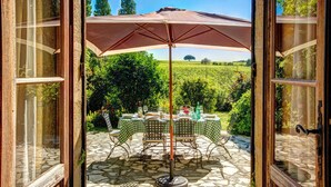 An open patio with a table set for dining, a large umbrella, and a view of a vineyard. - La Levaille - Four Bedroom Villa, Sleeps 8 (Landerrouat)