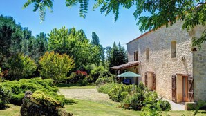 A stone building with a covered patio and a garden with various plants and trees. - La Levaille - Four Bedroom Villa, Sleeps 8 (Landerrouat)