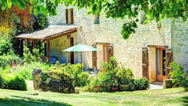 A stone building with a rustic thatched roof structure, a covered patio with a table and chairs, and a well-maintained garden with various plants and a large rock. - La Levaille - Four Bedroom Villa, Sleeps 8 (Landerrouat)