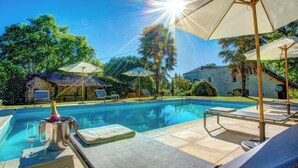 A swimming pool with lounge chairs and umbrellas, surrounded by trees and a stone building. - La Levaille - Four Bedroom Villa, Sleeps 8 (Landerrouat)