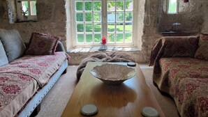 A rustic room with a large window, two sofas with patterned upholstery, a wooden table with decorative items, and stone walls. - Roc de Lapalue - Three Bedroom Villa, Sleeps 6 (Montcuq)