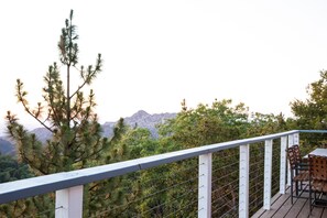 A balcony with a table and chairs, overlooking a mountainous landscape and dense trees. - UP and AWAY on Lake Arrowhead- Sleeps 6 & a cozy fireplace  (Lake Arrowhead)