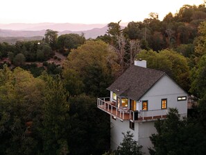 A white house with a balcony, surrounded by dense trees and hills in the background. - UP and AWAY on Lake Arrowhead- Sleeps 6 & a cozy fireplace  (Lake Arrowhead)