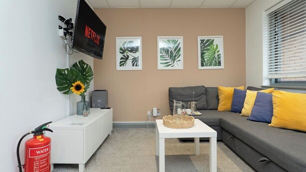 A living room with a grey sofa, white coffee table, and a mounted TV displaying 'NETFLIX'.
