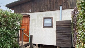 A rustic building with a wooden exterior and a small window. There is a wooden door and a set of steps leading to the entrance.