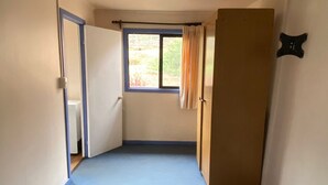 A room with a blue floor, a window with curtains, a ceiling fan, and a door.