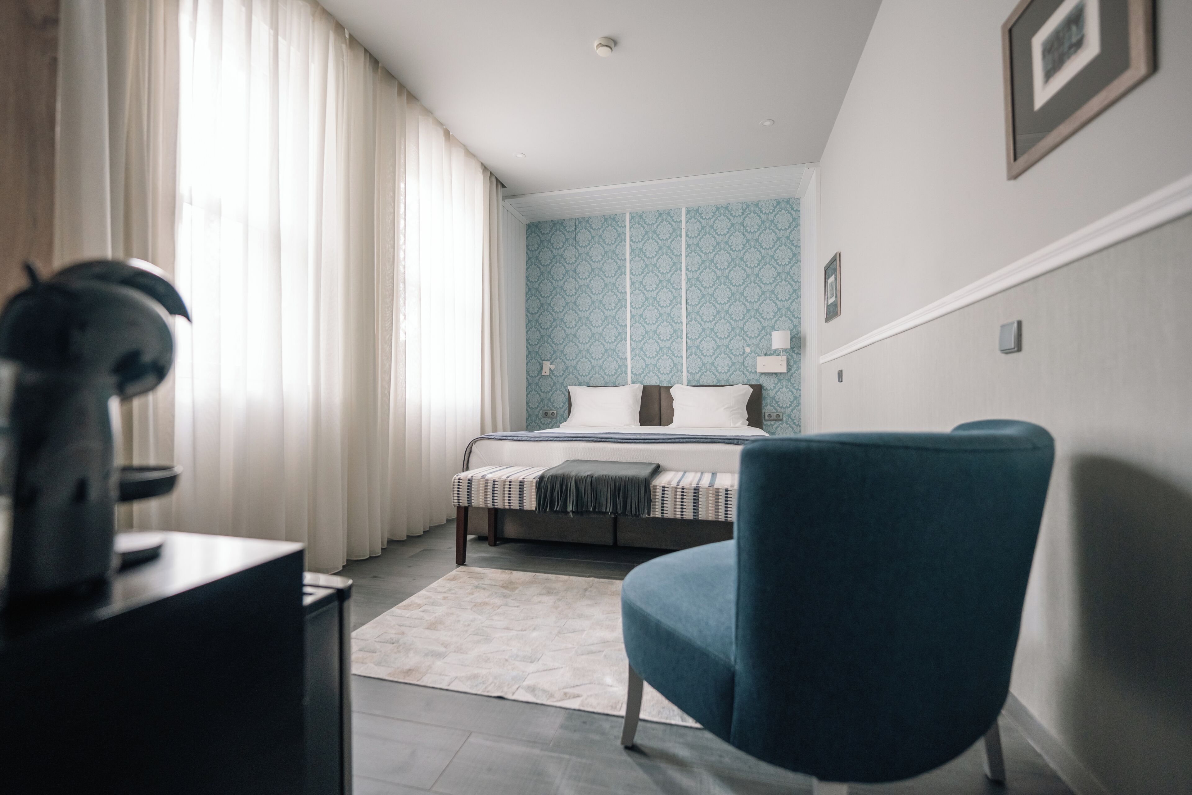 Un dormitorio con cama, una silla, un escritorio y una ventana con cortinas.