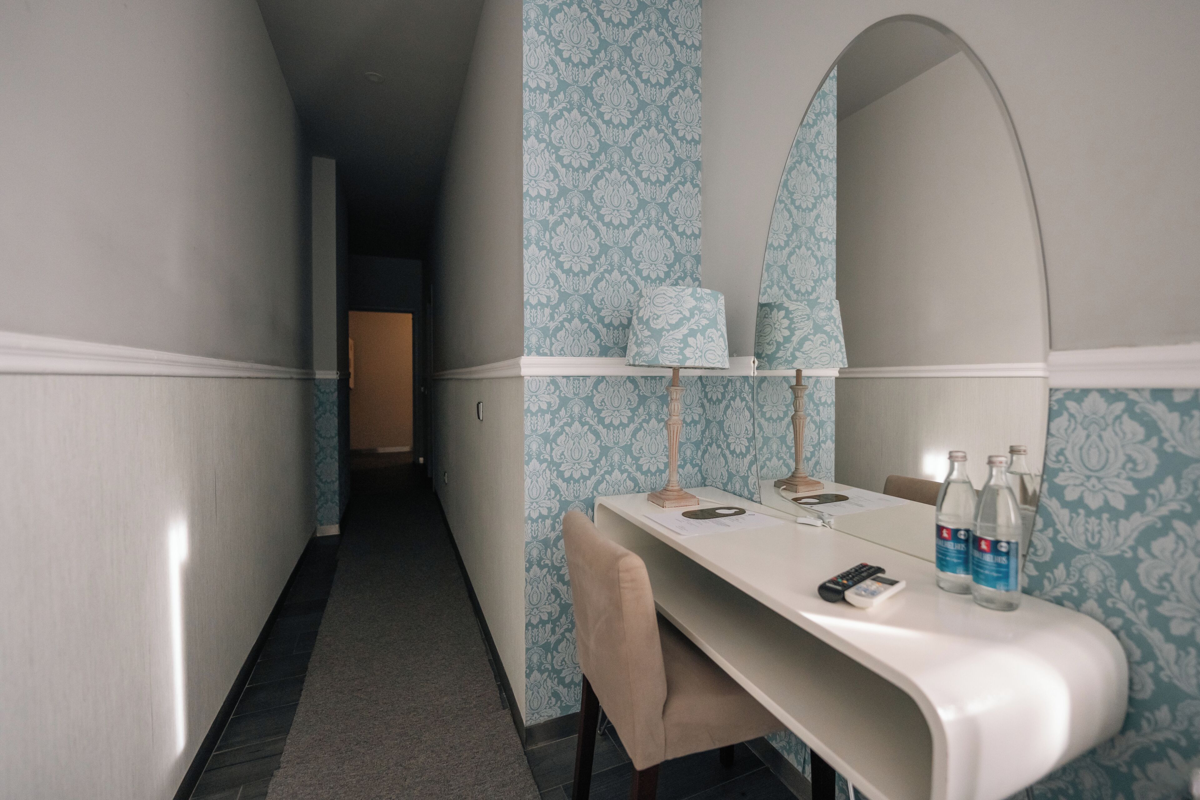 Ein Hotelzimmer mit Schminktisch, Spiegel, Tisch mit Stuhl und kleinem Schreibtisch mit Telefon und Flaschen.