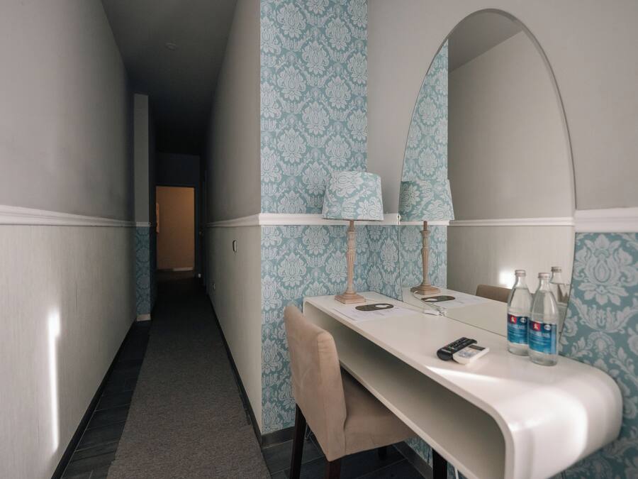 A hotel room with a vanity area, a mirror, a table with a chair, and a small desk with a phone and bottles.