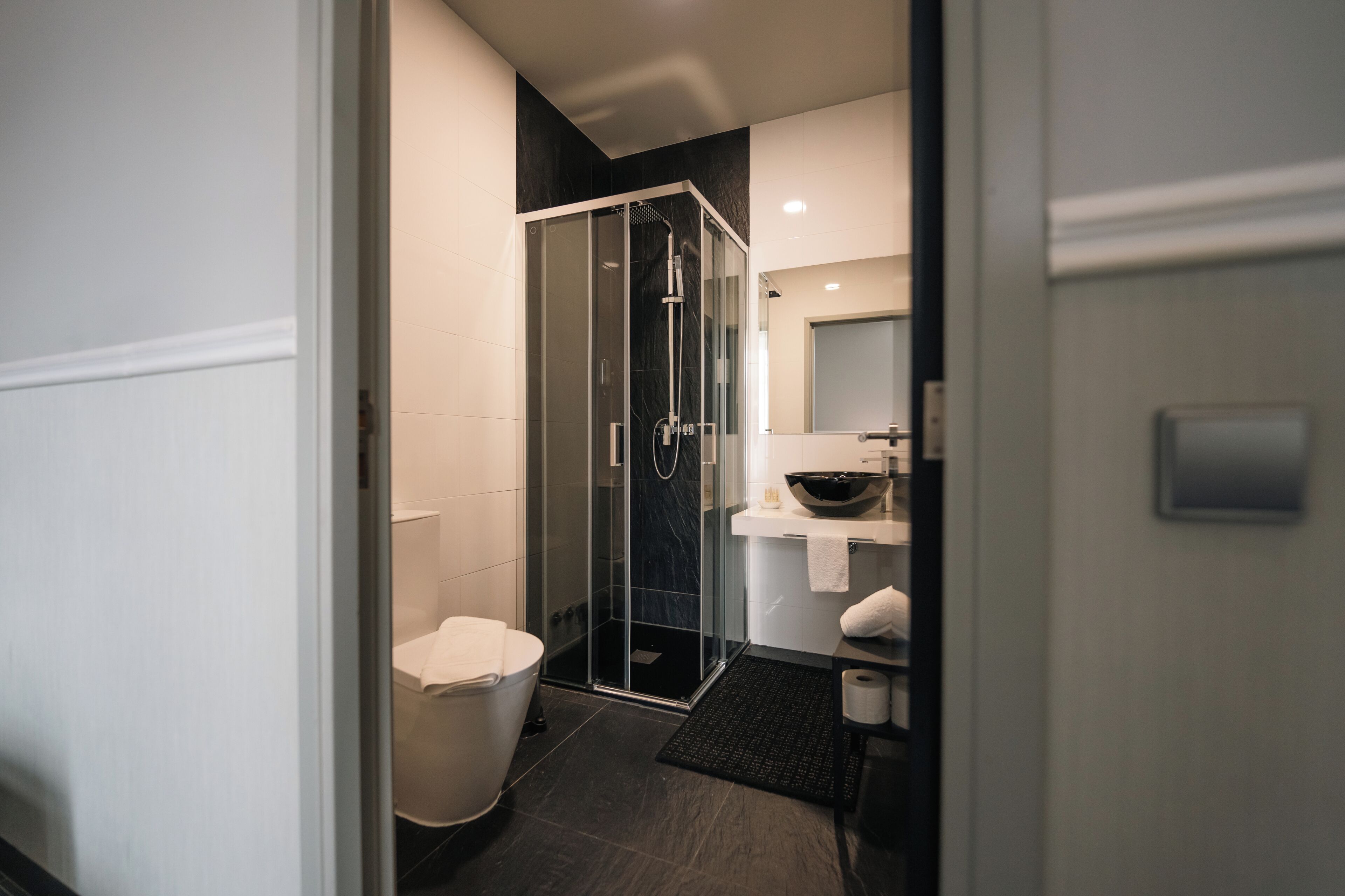 A modern bathroom with a glass shower enclosure, a white toilet, and a black bath mat.