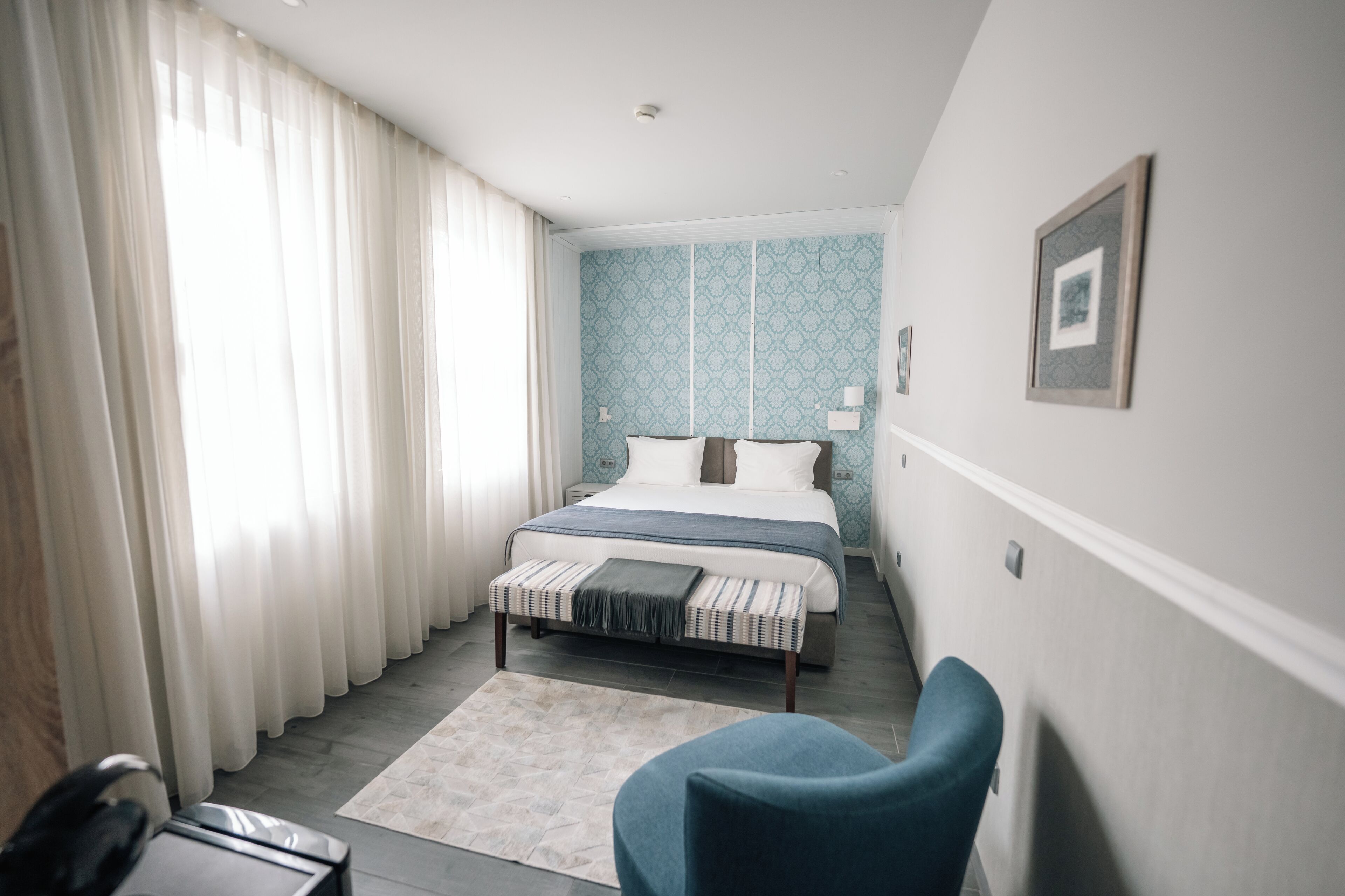 Une chambre d’hôtel avec un lit, une chaise, un bureau et une fenêtre avec des rideaux.