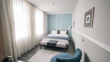 A hotel room with a bed, a chair, a desk, and a window with curtains.