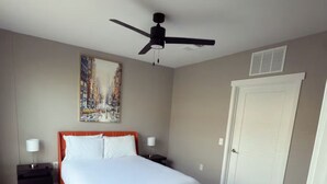 A bedroom with a bed, a ceiling fan, a painting, a nightstand, a lamp, and a door. - Charming Apartment with fitness room and in lovely Birmingham (Birmingham)
