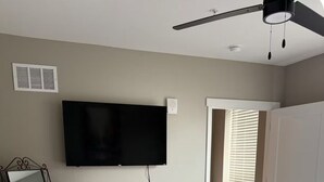 A bedroom with a bed, a ceiling fan, a TV mounted on the wall, a mirror, and a door leading to another room. - Charming Apartment with fitness room and in lovely Birmingham (Birmingham)