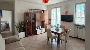A spacious living room with a dining area, a large cabinet, a TV, and a ceiling fan. - Casa Marta in Lucca within walking distance of downtown and hospital, private parking (Lucca)