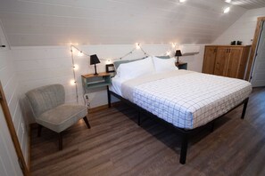 A bedroom with a bed, nightstands, a chair, and a wardrobe. - Private Woodland Greers Ferry Cottage w/ Fire Pit (Edgemont)