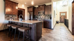 A modern kitchen with wooden cabinets, stainless steel appliances, and a large island with bar stools. - Park City Summer Retreat | Near Hiking, Biking & Jordanelle (Kamas)