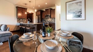 A modern kitchen with wooden cabinets, a central island, and a dining area with a glass table and chairs. - Park City Summer Retreat | Near Hiking, Biking & Jordanelle (Kamas)