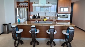 A modern kitchen with a central island, bar stools, stainless steel appliances, and wooden cabinetry. - Luxury apartment on the beach with beautiful views (Puerto Vallarta)
