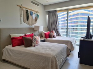 Ein Hotelzimmer mit zwei Betten, einem Schreibtisch, einem Fernseher und einem großen Fenster mit Blick auf ein modernes Gebäude.