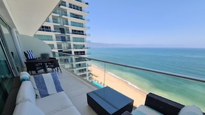 A balcony with a sofa, a table, and a chair overlooking a beach and ocean. - Luxury apartment on the beach with beautiful views (Puerto Vallarta)