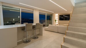 A modern living area with a kitchen, bar stools, a sofa, a TV, and a staircase.