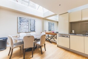 A modern kitchen with a skylight, a dining area with a wooden table and chairs, and a large abstract painting on the wall. - Stylish Chelsea Escape with Charm (London)