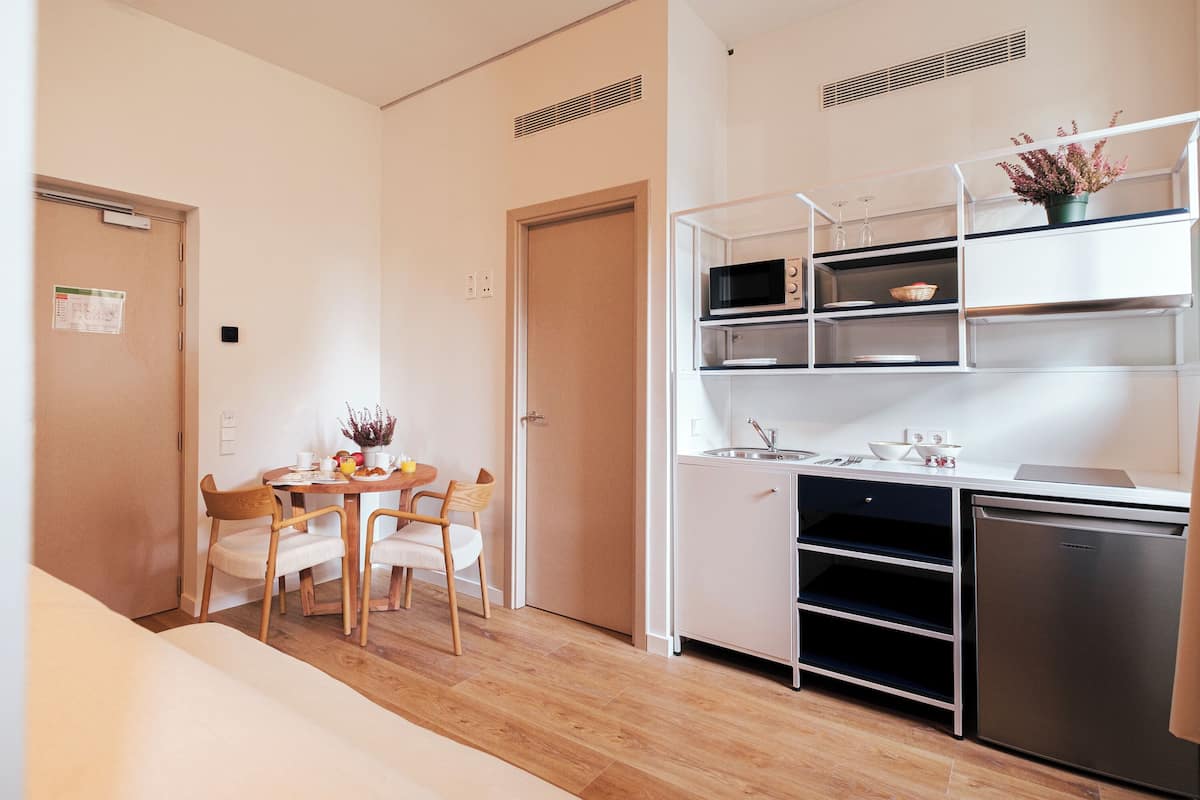 A compact kitchen with a microwave, sink, and a refrigerator. There is a dining area with a table and chairs.