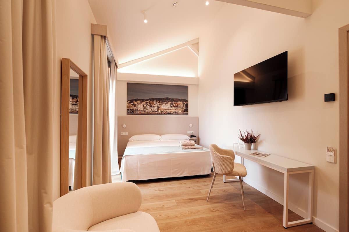A modern bedroom with a bed, a desk, a chair, a TV, and a painting on the wall.