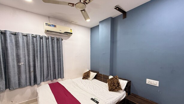 Een slaapkamer met een bed, een plafondventilator, een airconditioning en een nachtkastje met een stopcontact.