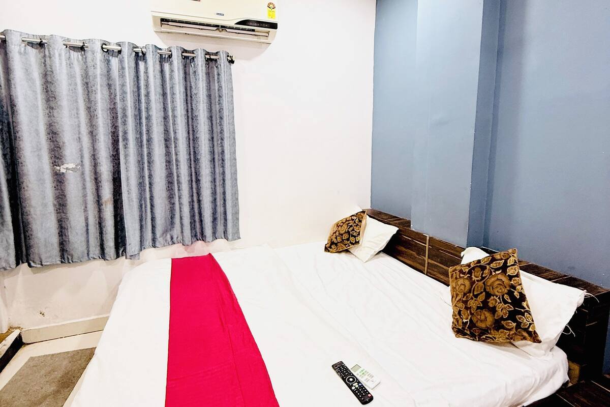 Een slaapkamer met een bed, een plafondventilator, een airconditioning en een raam met gordijnen.