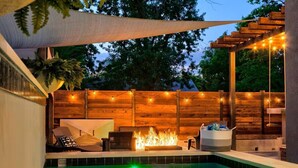 Área de piscina com lareira, deck de madeira e luzes de corda.