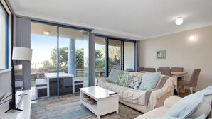 A modern living room with a sofa, coffee table, and dining area. - Nautilus 2 Ground Floor Apartment (Hawks Nest)