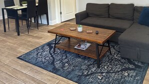 Una sala de estar con un sofá, una mesa de centro, una mesa de comedor con sillas, un reloj y un cuadro en la pared.