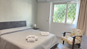 A neatly made bed with a grey headboard, a bedside table with a lamp, and a chair with a floral pattern. - C Room with shared bathroom; Sweet Home Fleming (Roma)
