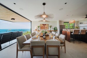 A dining area with a view of the ocean, a large table set for six, and a bar area with chairs. - Villa Zest 4 bedroom Villa • Rooftop Infinity Pool & Ocean Views (manuel antonio)
