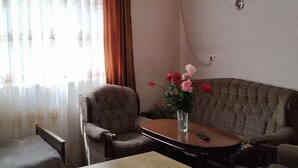A living room with a sofa, armchairs, a coffee table, and a dining table. There is an air conditioning unit on the wall and a ceiling light fixture. - 21 Apartment in Yerevan 01 (Yerevan)