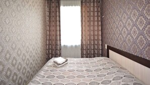 A bedroom with patterned wallpaper, a bed with a patterned bedspread, and a window with curtains. - 21 Apartment in Yerevan 3 (Yerevan)