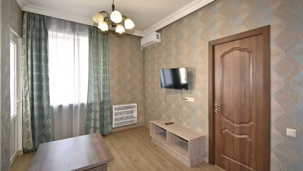 A room with a wooden door, a mounted TV, a bench, and a table. - 21 Apartment in Yerevan 3 (Yerevan)
