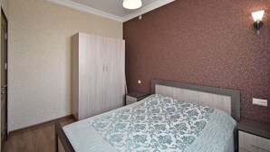 A bedroom with a bed, a wardrobe, a nightstand, and a wall-mounted light fixture. - 21 Apartment in Yerevan 1 (Yerevan)