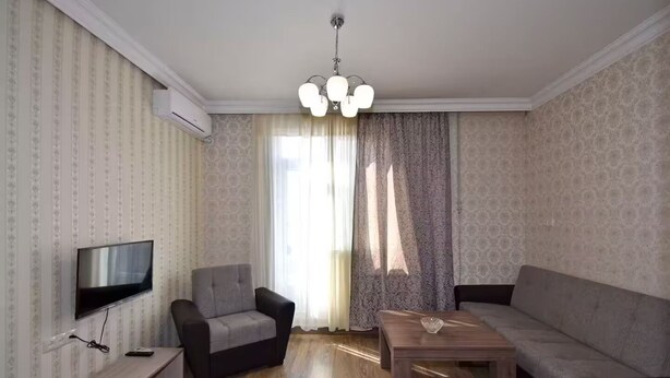 A living room with a flat-screen TV, two armchairs, a sofa, a wooden coffee table, and a chandelier. - 21 Apartment in Yerevan 1 (Yerevan)