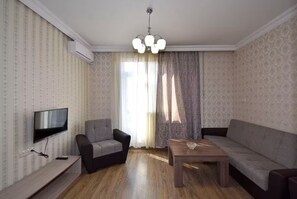 A living room with a flat-screen TV, two armchairs, a sofa, a wooden coffee table, and a chandelier. - 21 Apartment in Yerevan 1 (Yerevan)