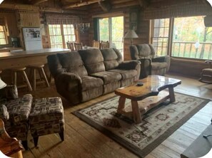 Ein gemütliches Blockhaus-Interieur mit einem Holzesstisch, zwei Sofas und einem gemusterten Teppich.